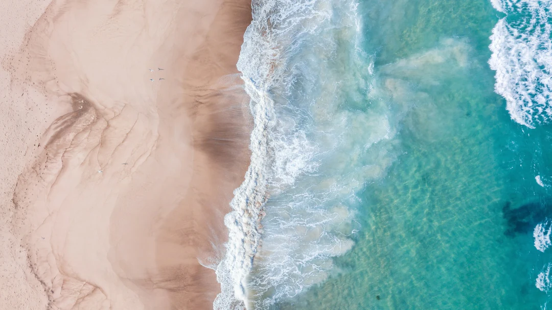 Aerial view of pale sand and turquoise surf in a 16:9 frame